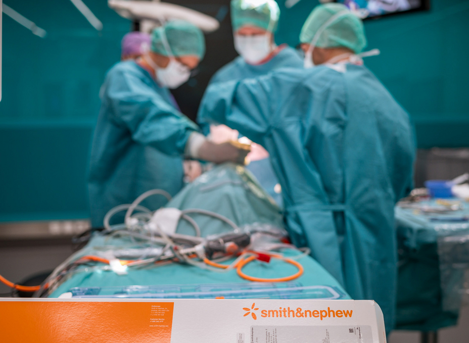 Three surgeons work at an operating table as part of a cruciate ligament surgery course in the OR-X. A Smith+Nephew product pack is in the foreground.