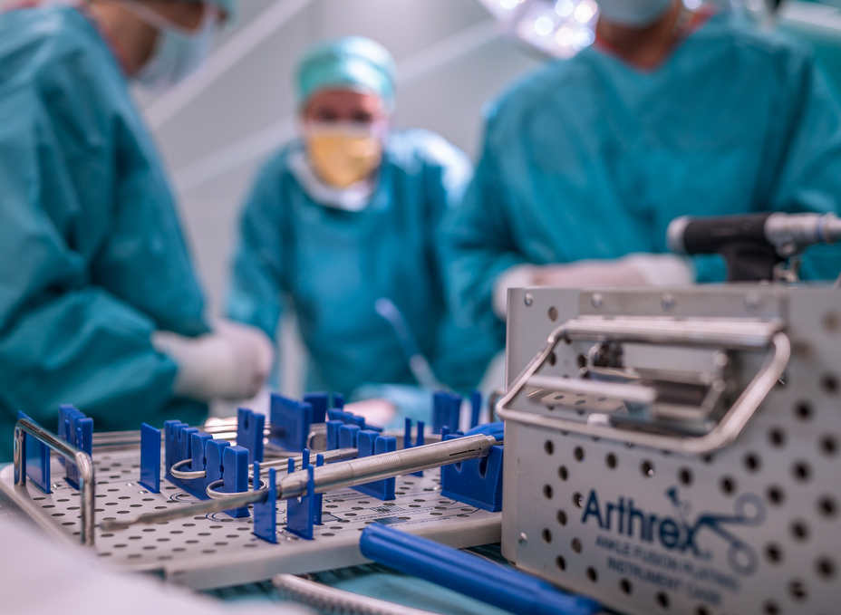 Arthrex instruments for minimally invasive surgery lie on the table in the OR-X, while a group of surgeons discuss in the background.