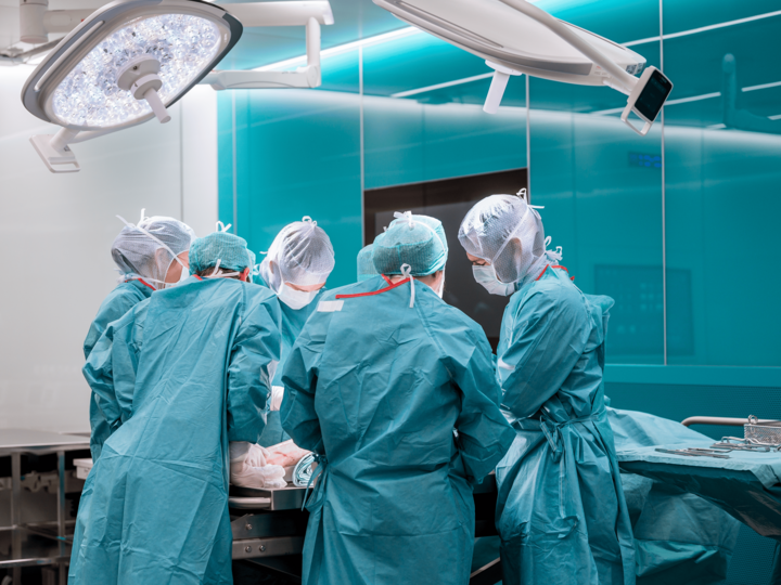  A group of four residents stand around an operating table and perform a surgical procedure.