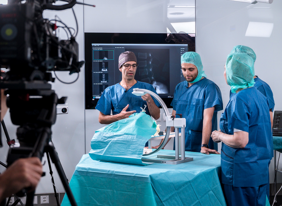 Prof. Mazda Farshad and Dr. Hooman Esfandiari explain to Dr. Jeanne Fürst how the X23D technology works using a C-arm model.