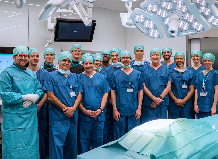 The participants of the first Surgical Data Science Workshop stand for a group picture in the OR-X, wearing surgical scrubs clothing.