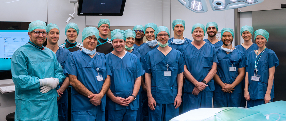 The participants of the first Surgical Data Science Workshop stand for a group picture in the OR-X, wearing surgical scrubs clothing.
