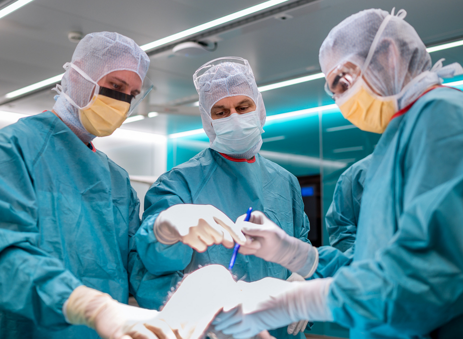 Three surgeons dressed in surgical clothing discuss access to the knee joint in the OR-X
