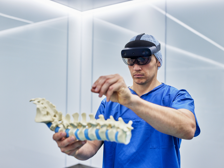 A surgeon wearing an AR headset in the OR, holding a spine model in his hand.