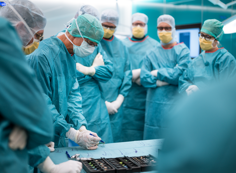 A hand surgeon draws a sketch on the surgical drape in front of a group of residents to illustrate the approaches to the wrist