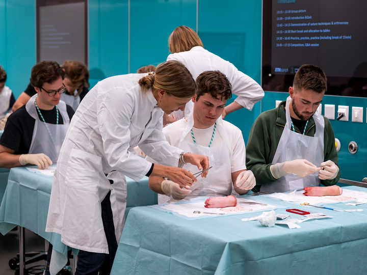 A surgeon shows two medical students how to perform a surgical suture.